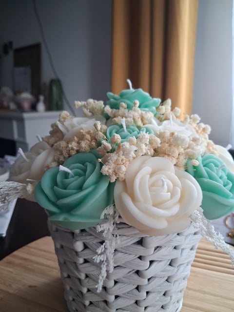 Decorative floral arrangement with white and turquoise roses and small cream flowers in a woven white basket container