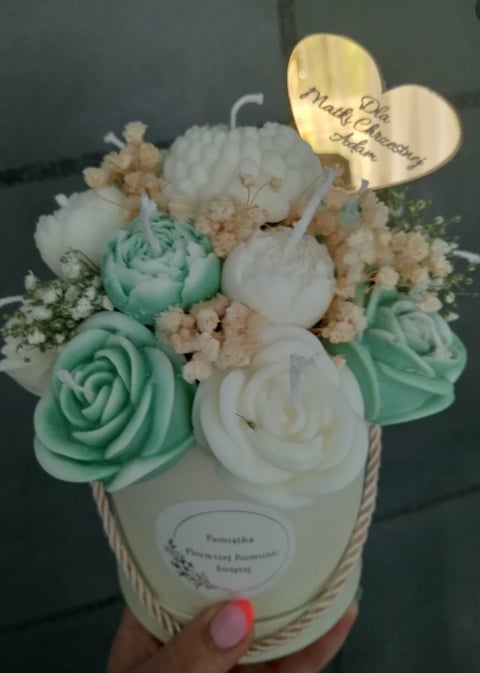 Floral arrangement in white container with mint green and white roses, white peonies, and babys breath, topped with decorative wooden tags, held in hand