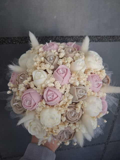 Bridal bouquet with white, pink, and taupe roses, babys breath, and white feather accents held against a gray background